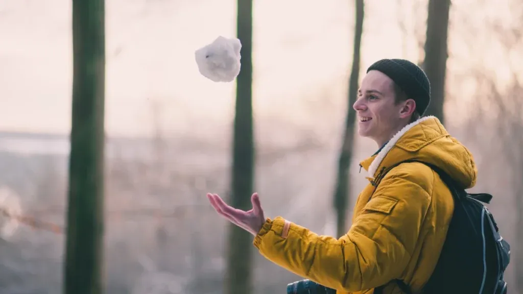 Man med gul vinterjacka som kastar snöboll